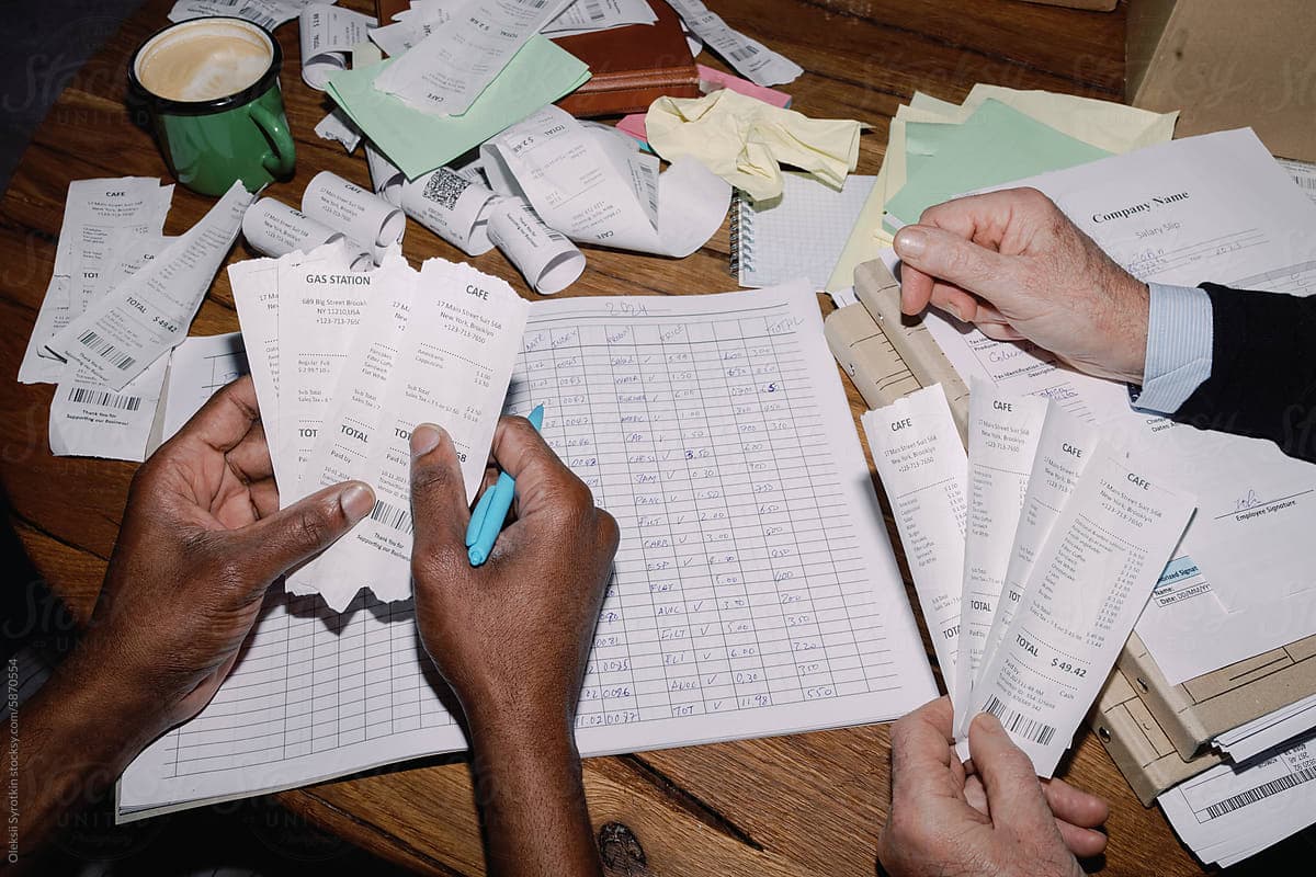 Two people comparing receipts, forms, and spreadsheets on a table